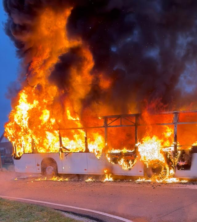 Das Bild zeigt Einsatzkräfte am ausgebrannten Linienbus.