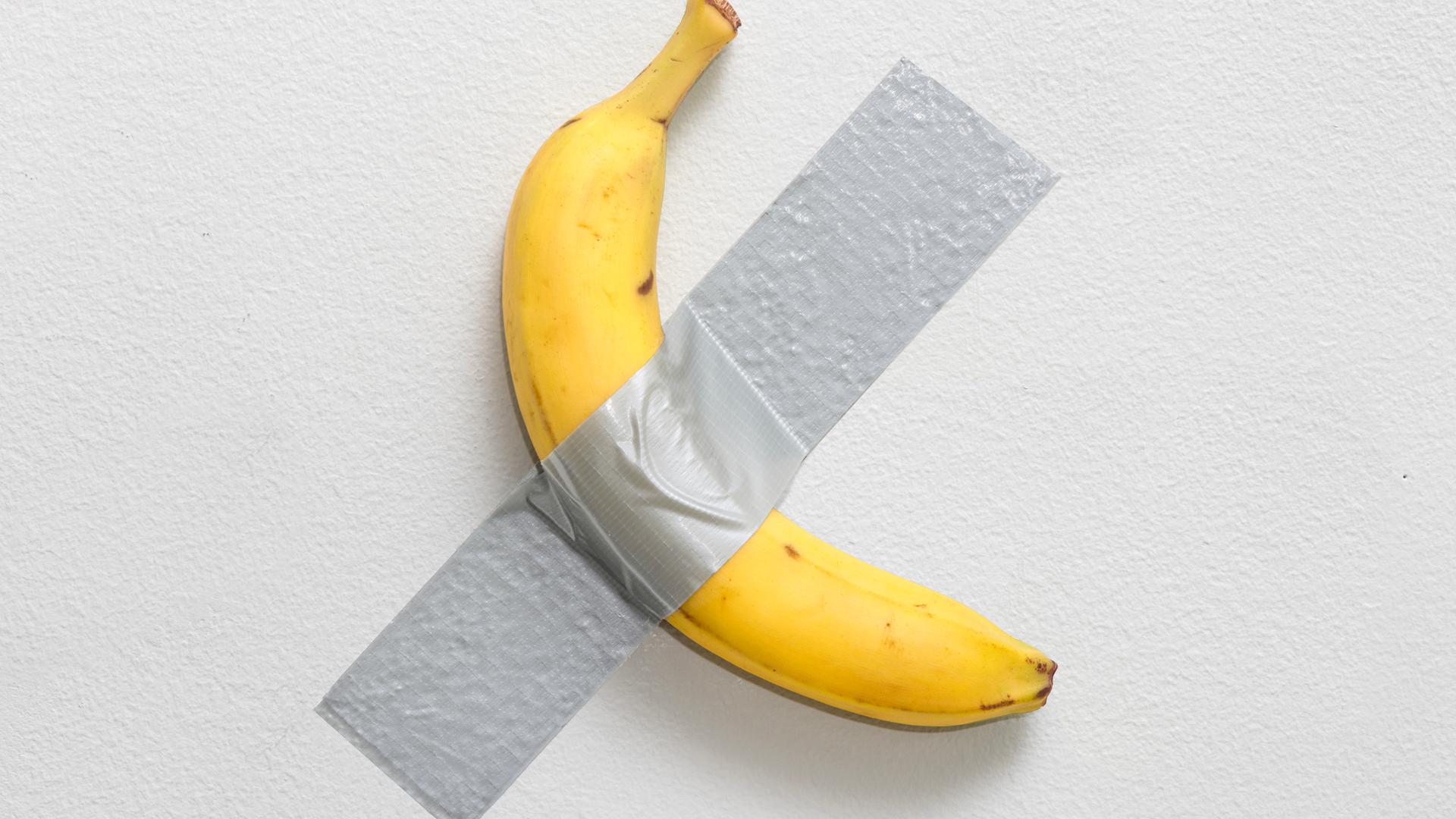 Eine Banane klebt mit Klebeband auf einer Wand.