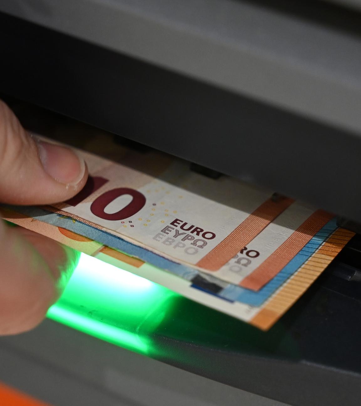 Ein Mann zieht Geldscheine aus de, Ausgabefach eines Geldautomaten. (Archiv)