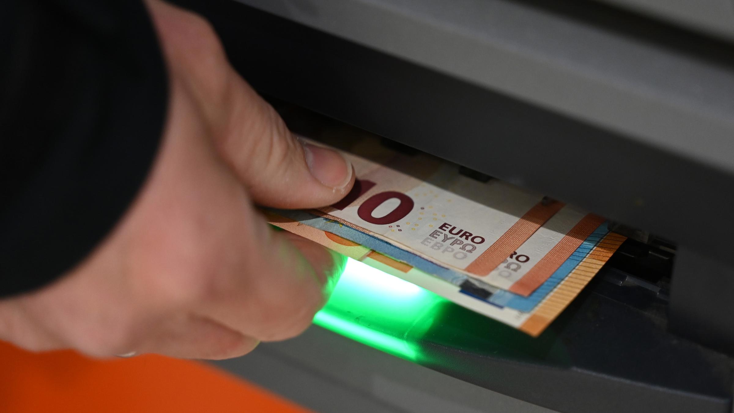 Ein Mann zieht Geldscheine aus de, Ausgabefach eines Geldautomaten. (Archiv)