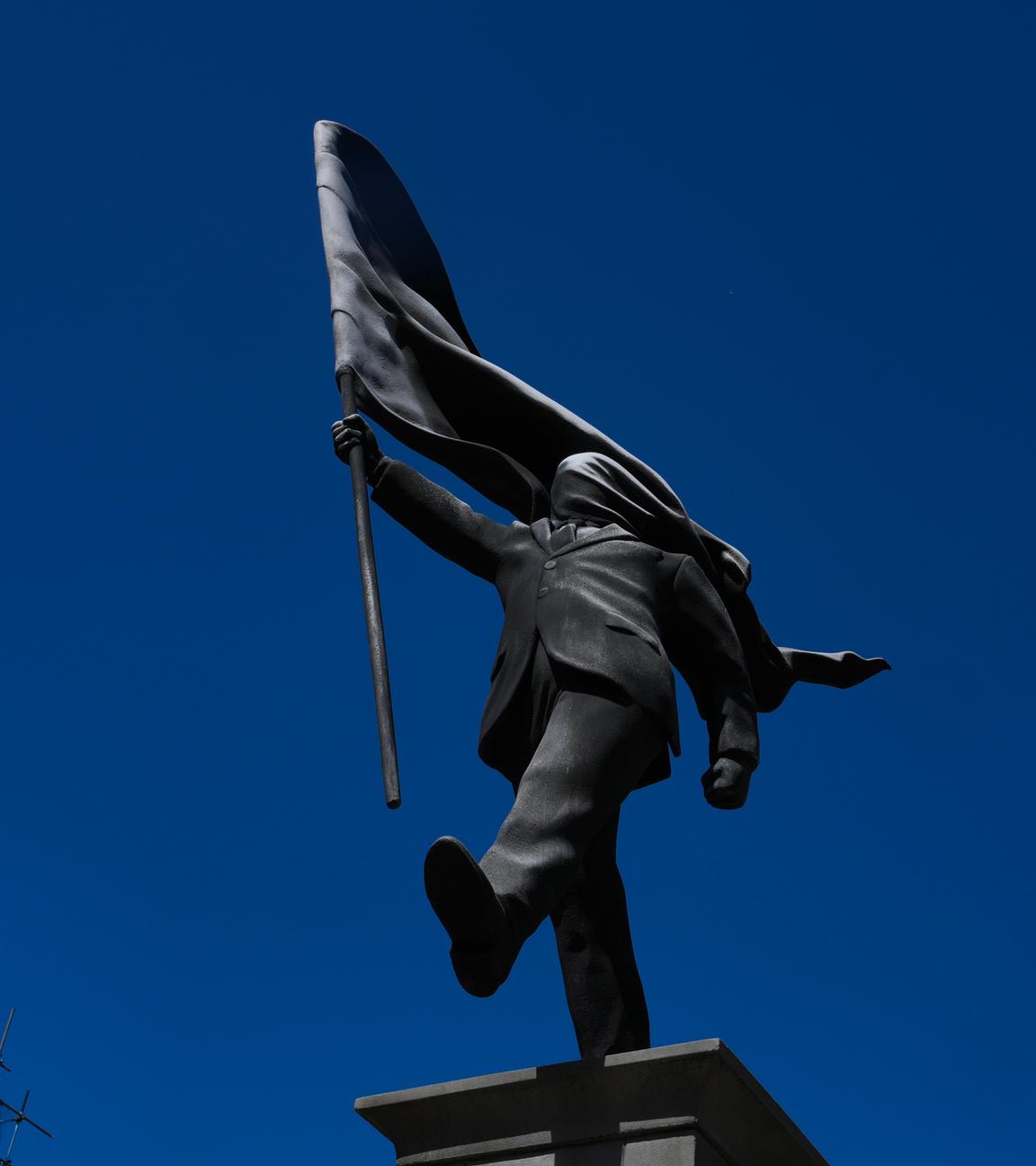 Eine Statue eines Mannes, der eine Fahne vor sein Gesicht hält und mit „Banksy“ signiert ist; sie ist am Waterloo Place in London aufgetaucht.