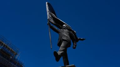 Eine Statue eines Mannes, der eine Fahne vor sein Gesicht hält und mit „Banksy“ signiert ist; sie ist am Waterloo Place in London aufgetaucht.
