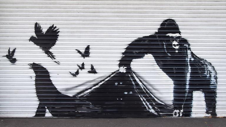Ein Garagentor, auf dem ein Graffiti zu sehen ist, das einen Gorilla zeigt, der scheinbar das Garagentor wie einen vorhang anhebt und einen Seehund, Vögel und Fledermäuse frei lässt.