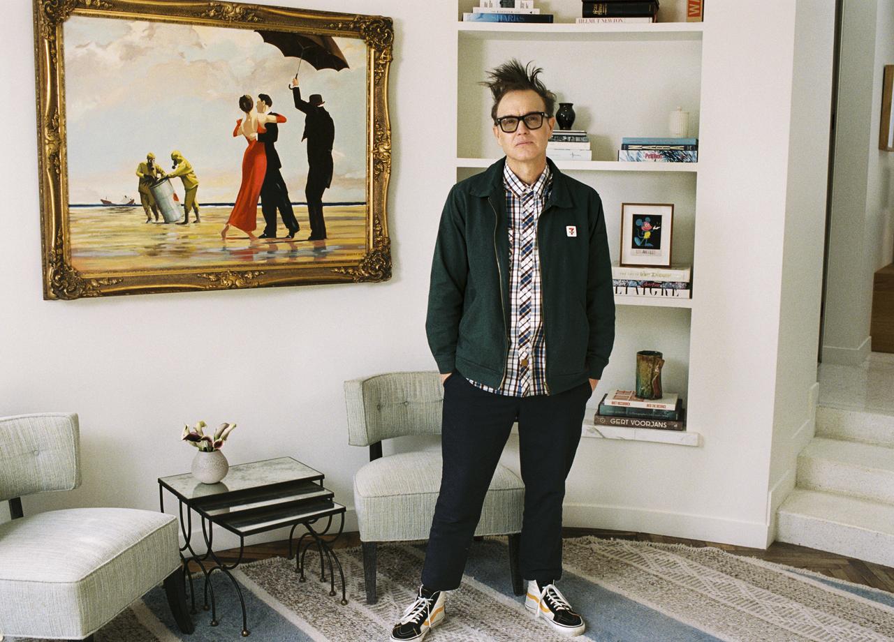 Der Blink-182-Musiker Mark Hoppus steht neben dem Öl-Gemälde von Banksy auf dem zwei Menschen in Abendgaderobe tanzen, im Hintergrund sind zwei Menschen in Schutzanzügen zu sehen, die scheinbar Giftmüll oder Ähnliches entsorgen.