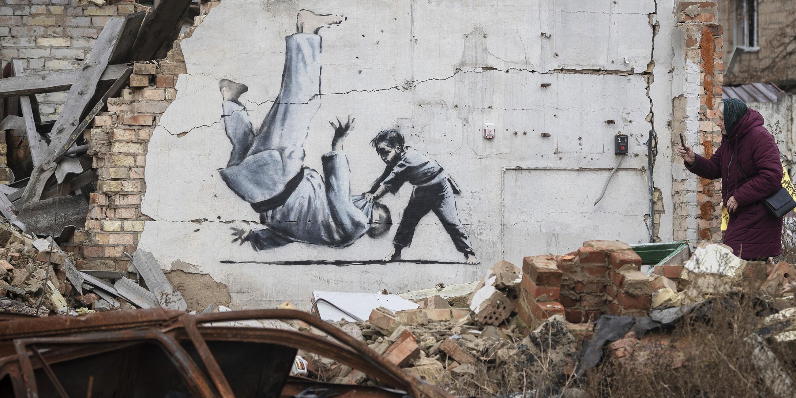 Eine Frau fotografiert am 13.11.2022, ein Kunstwerk, das möglicherweise vom britischen Straßenkünstler Banksy an einem durch Kämpfe zerstörten Gebäude in Borodyanka in der Region Kiew in der Ukraine angefertigt wurde.
