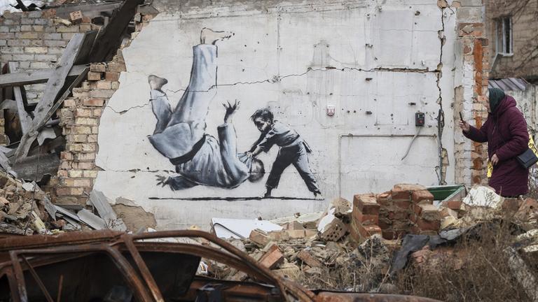Eine Frau fotografiert am 13.11.2022, ein Kunstwerk, das möglicherweise vom britischen Straßenkünstler Banksy an einem durch Kämpfe zerstörten Gebäude in Borodyanka in der Region Kiew in der Ukraine angefertigt wurde.