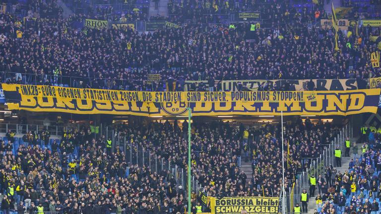 Fans von Borussia Dortmund halten einen großen Banner in der Fankurve nach oben am 08.11.2025.