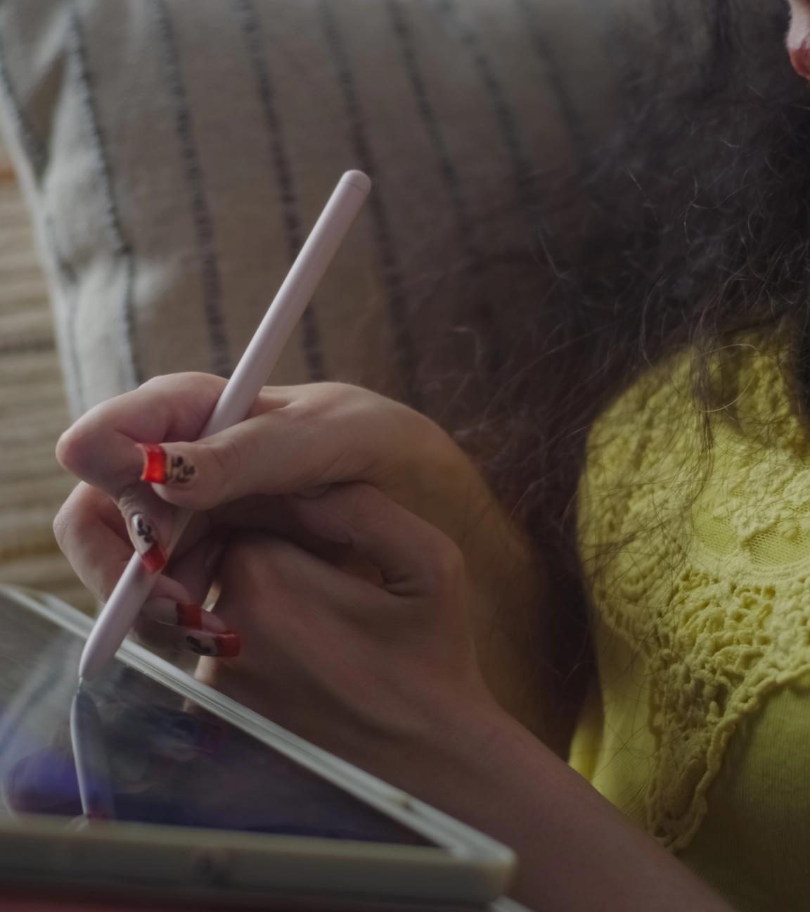 Frau mit Tablet sitzt auf dem Sofa und führt mit der einen Hand die andere, um mit einem Stift eine Eingabe auf dem Bildschirm zu machen.