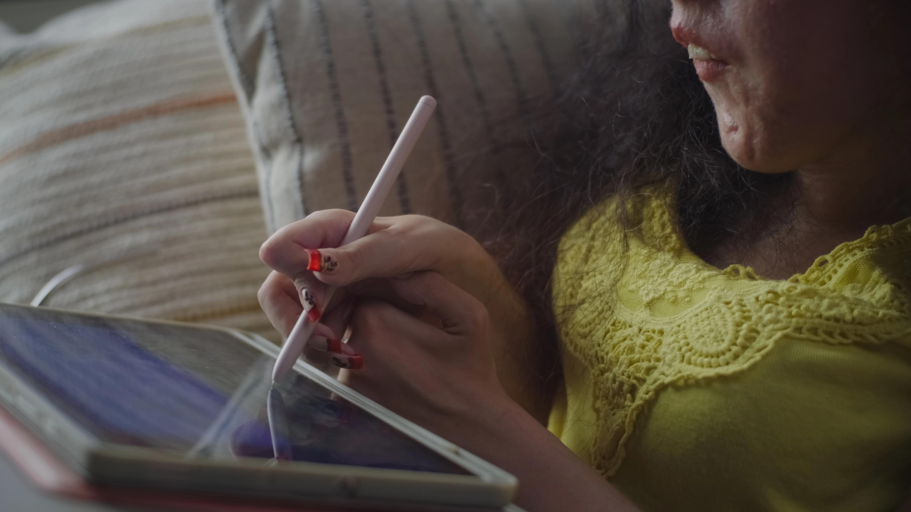 Frau mit Tablet sitzt auf dem Sofa und führt mit der einen Hand die andere, um mit einem Stift eine Eingabe auf dem Bildschirm zu machen.