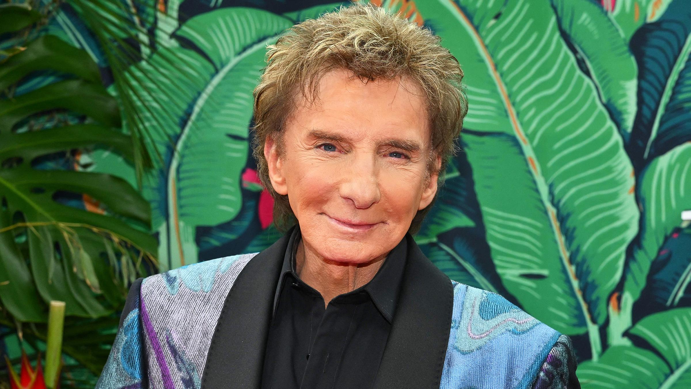 Barry Manilow posiert vor großen grünen Blättern.