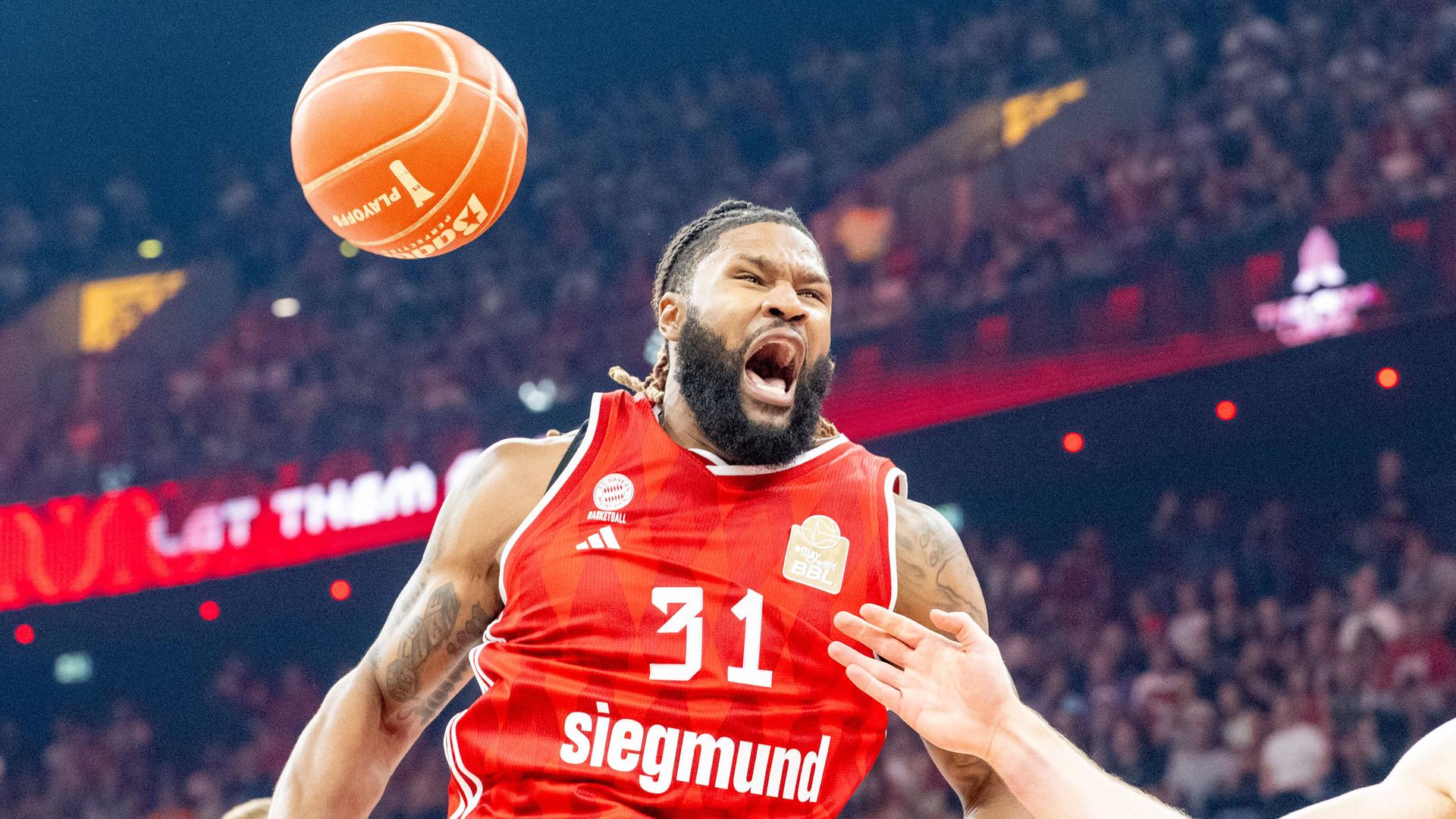 Devin Booker von FC Bayern Basketball brüllt während dem Spiel gegen Ratiopharm Ulm. Ein Basketball fliegt neben seinem Kopf vorbei.