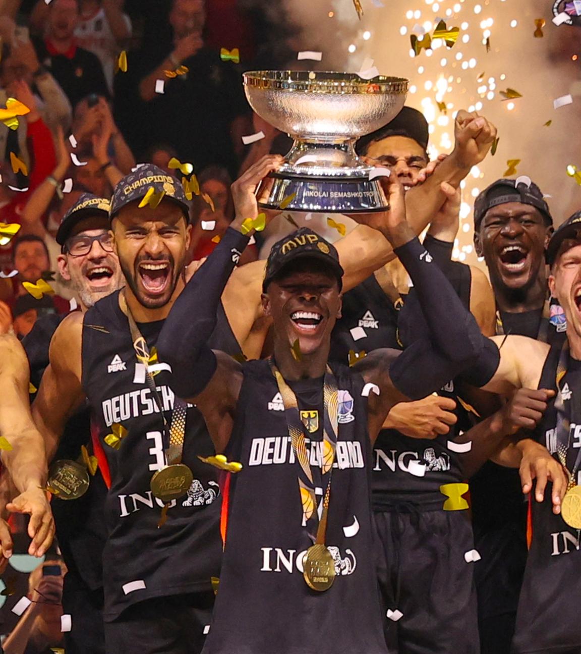 die jubelnde Nationalmannschaft. Der Kapiätan der Mannschaft Dennis Schröder hebt den Pokal in die Luft. Es fliegt goldenes Konfetti