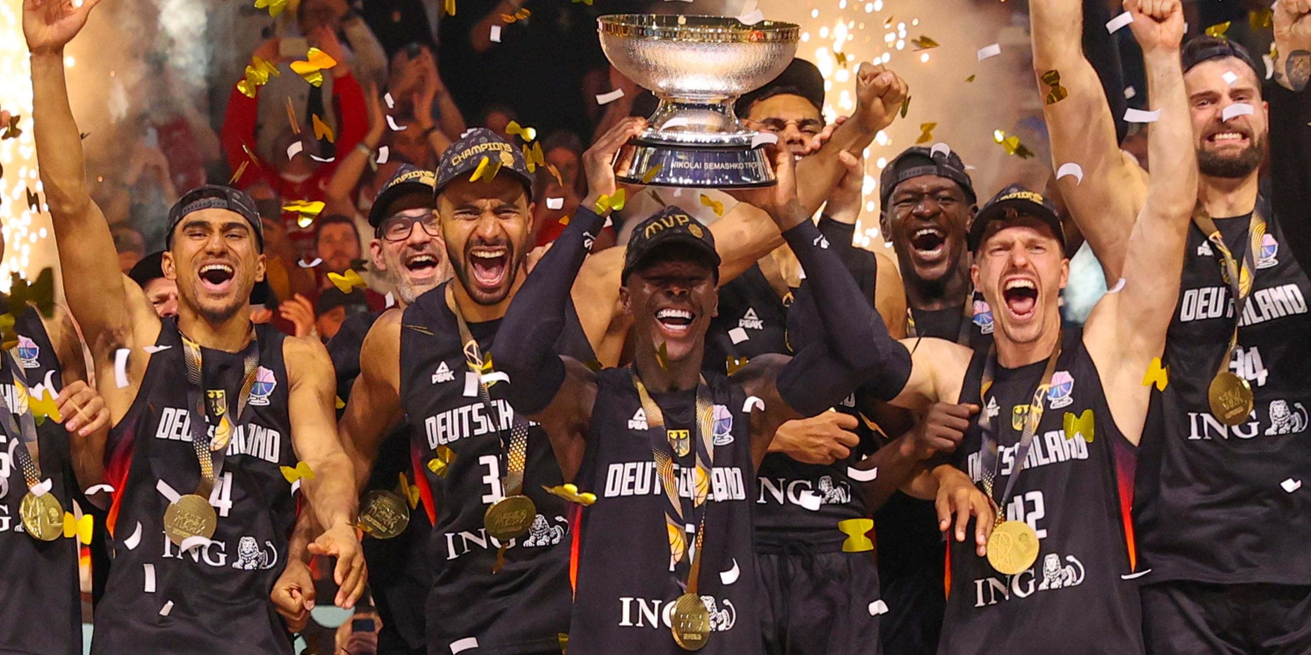 die jubelnde Nationalmannschaft. Der Kapiätan der Mannschaft Dennis Schröder hebt den Pokal in die Luft. Es fliegt goldenes Konfetti