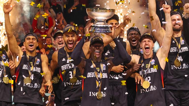 die jubelnde Nationalmannschaft. Der Kapiätan der Mannschaft Dennis Schröder hebt den Pokal in die Luft. Es fliegt goldenes Konfetti