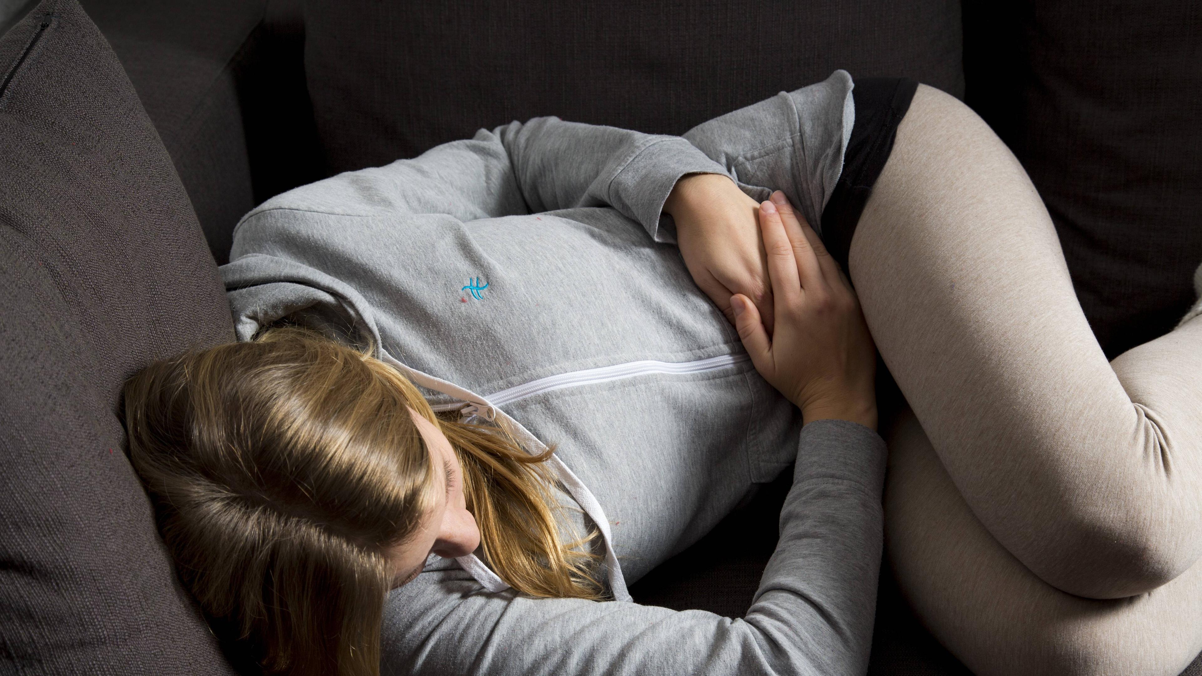Frau liegt auf dem Sofa und hält sich den Bauch.