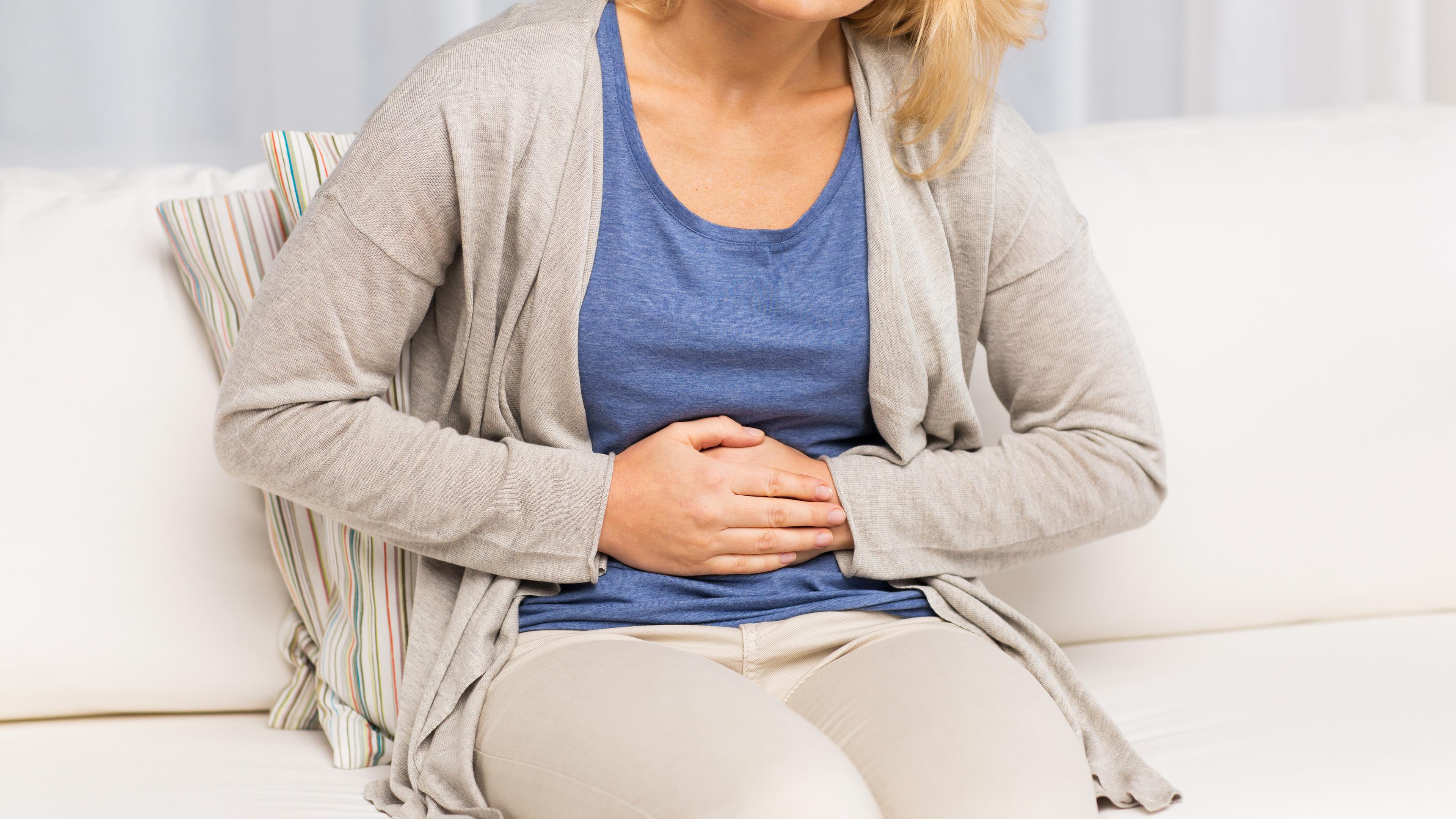 Eine Frau hält sich sitzend unter Schmerzen den Bauch.