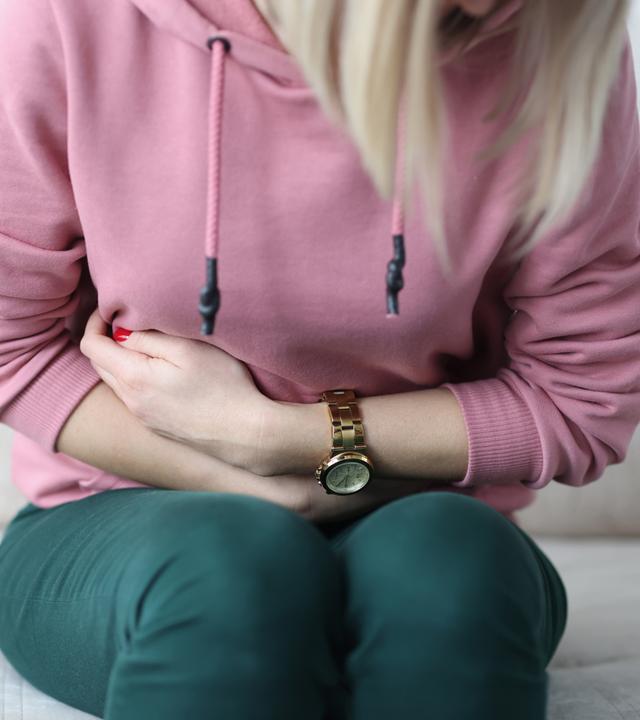 Eine Frau sitzt gekrümmt auf einem Sofa und hält sich den Bauch.
