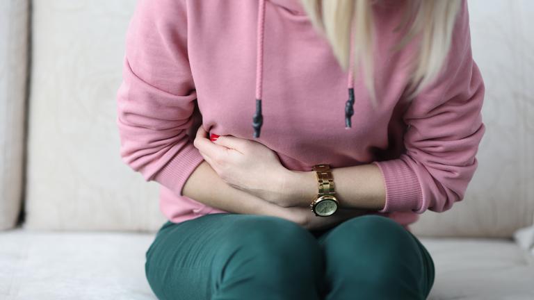 Eine Frau sitzt gekrümmt auf einem Sofa und hält sich den Bauch.