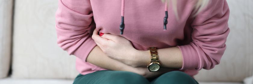 Eine Frau sitzt gekrümmt auf einem Sofa und hält sich den Bauch.