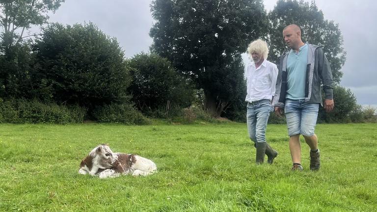 Jetziger Landwirt Remi Hardy und der Mann der neuen Landwirtin Corinne Beaujean auf einer wiese mit einem Rind.