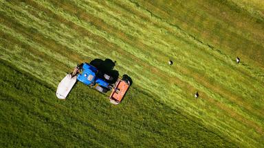 Ein Landwirt fährt mit seinem Traktor und einem angebauten Mähwerk über eine Wiese und mäht diese.