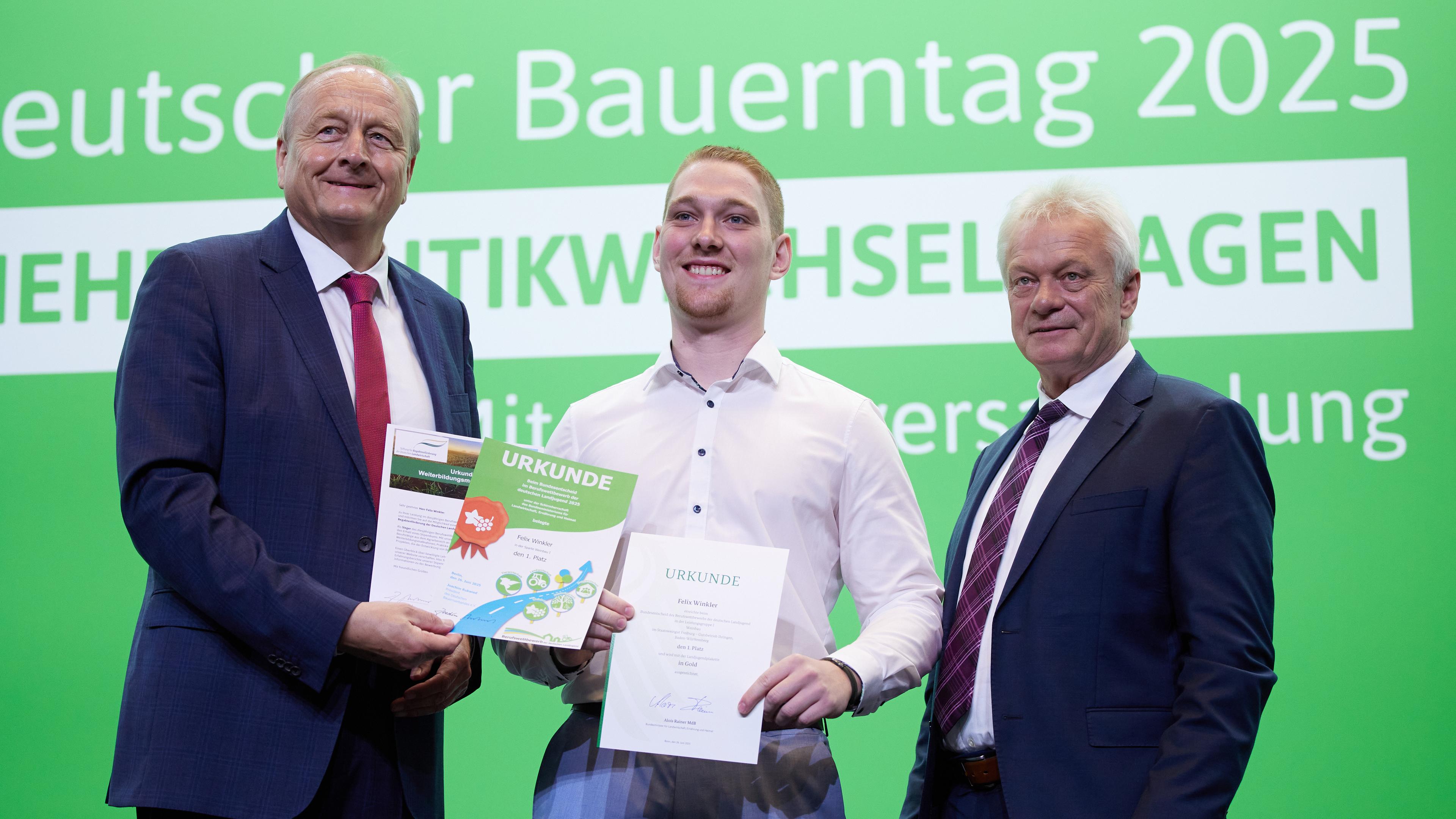 oachim Rukwied (l), Präsident des Deutschen Bauernverbands , und Alois Rainer (CSU), Bundeslandwirtschaftsminister, gratulieren Felix Winkler aus Rheinland Pfalz zum Sieg beim Berufswettbewerb der Deutschen Landjugend in der Sparte Weinbau auf einer Bühne.