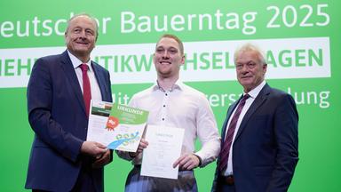 oachim Rukwied (l), Präsident des Deutschen Bauernverbands , und Alois Rainer (CSU), Bundeslandwirtschaftsminister, gratulieren Felix Winkler aus Rheinland Pfalz zum Sieg beim Berufswettbewerb der Deutschen Landjugend in der Sparte Weinbau auf einer Bühne.