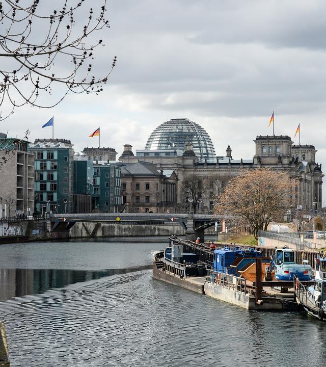 Auf einer Arbeitsplattform werden ein Bagger und ein eingeklappter Kran auf der Spree von einer Baustelle am Schiffbauerdamm in Richtung Reichstag weggefahren.
