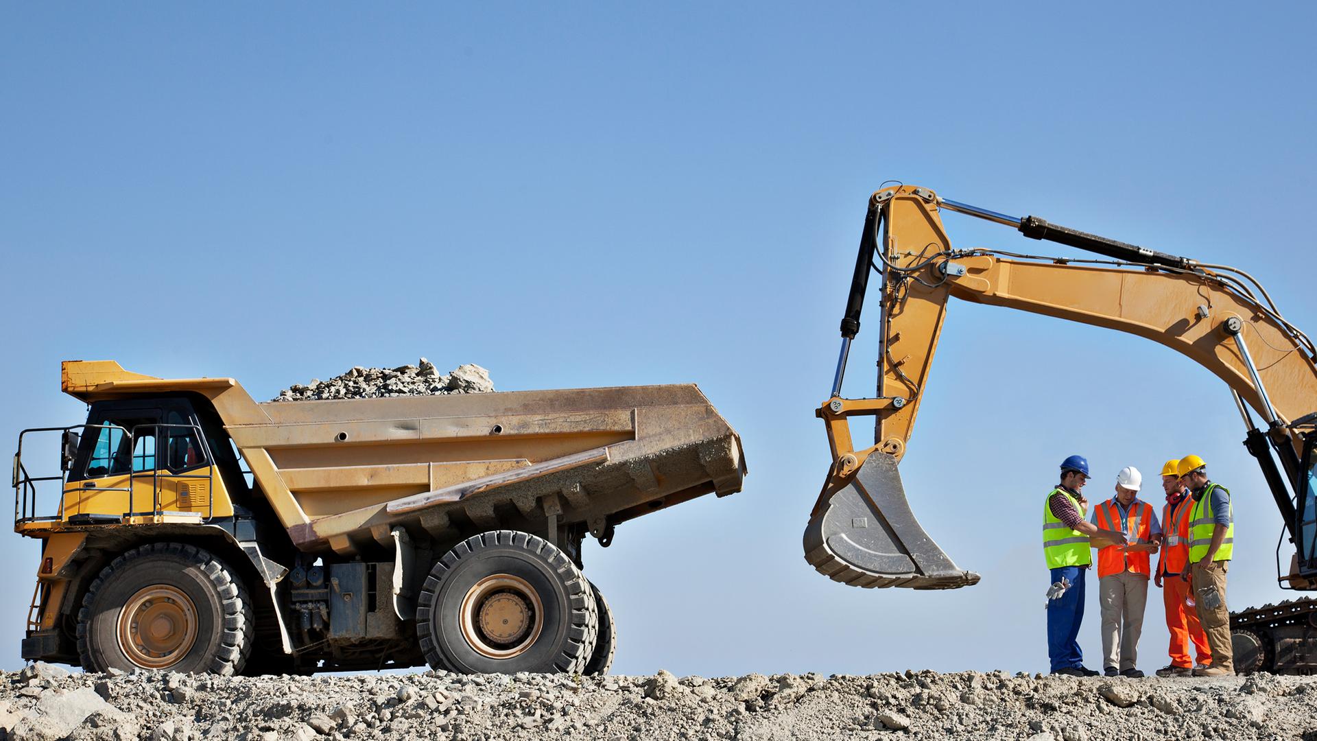 Bauarbeiter besprechen sich neben einem Bagger und einem Laster