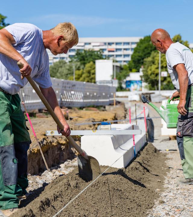 Zwei Bauarbeiter sind auf einer Baustelle, der Himmel ist blau.
