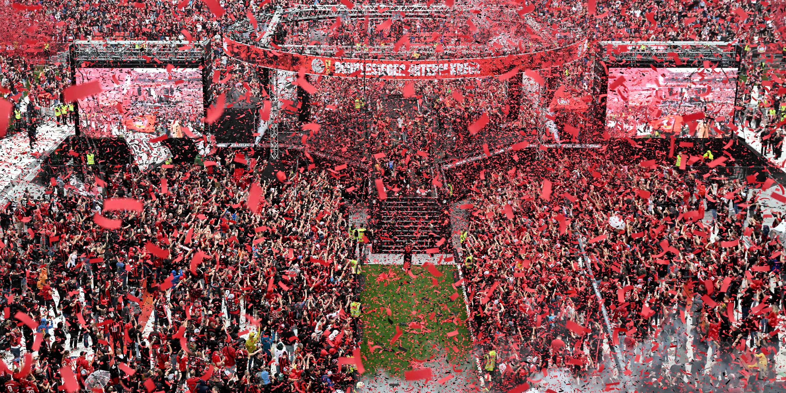 Spieler und Fans von Bayer Leverkusen feiern den Gewinn der Bundesliga und des DFB-Pokals im Stadion während der Siegesfeier.