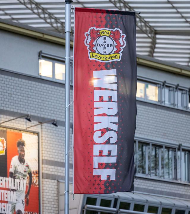 Eine Flagge mit den Farben und dem Wappen von Bayer 04 Leverkusen und der Aufschrift "Werkself" vor der BayArena.