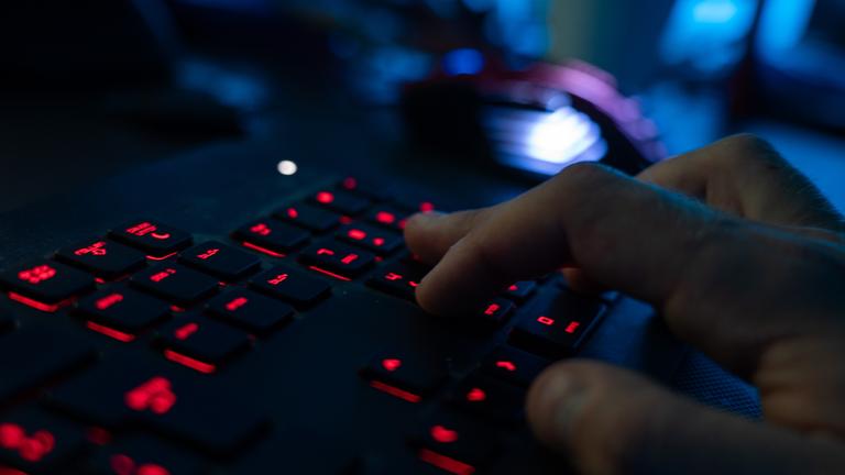 Eine rot beleuchtete Tastatur in dunklem, bläulichen Licht, eine rechte Hand schreibt auf der Tastatur.