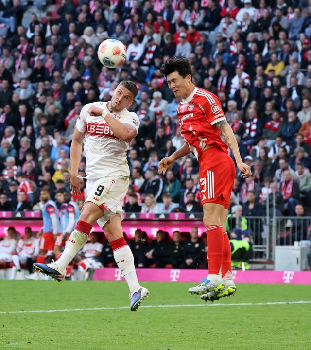 Ermedin Demirovic (VfB Stuttgart) und Minjae Kim (FC Bayern München) springen Seite an Seite in Richtung Ball