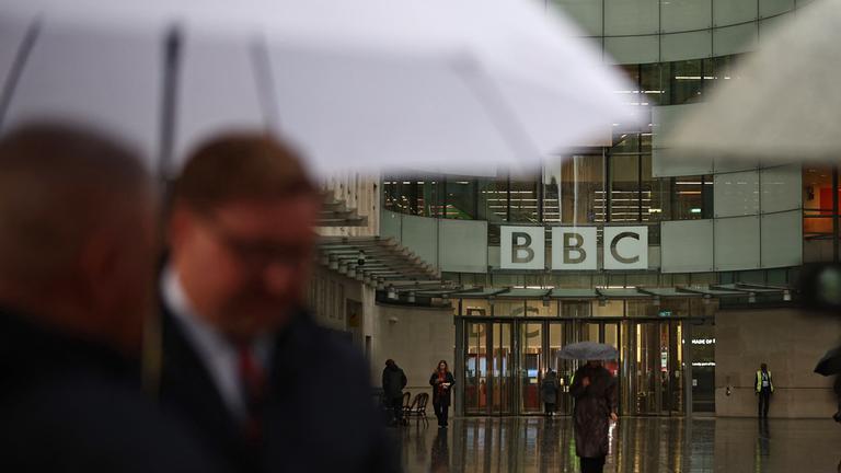 People shelter from the rain outside the entrance to the BBC in London on November 10, 2025.