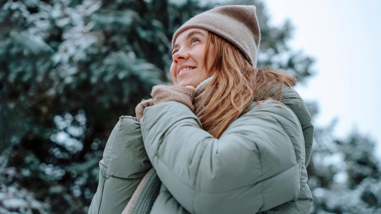 Frau mit Winterjacke und Mütze steht in verschneiter Landschaft.