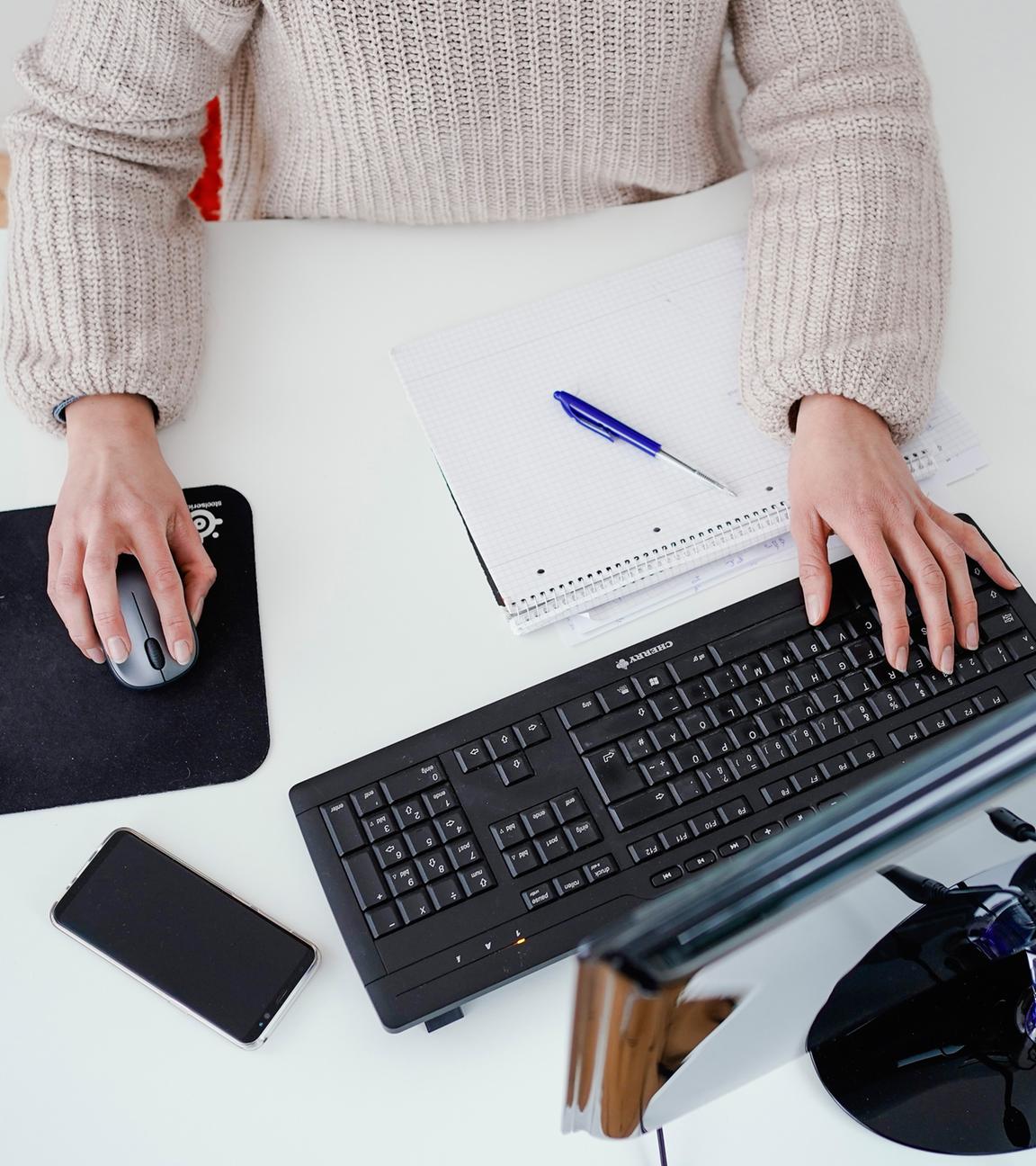 Eine Frau arbeitet an einem Stehtisch und betätigt die Maus und Tastatur eines Computers.