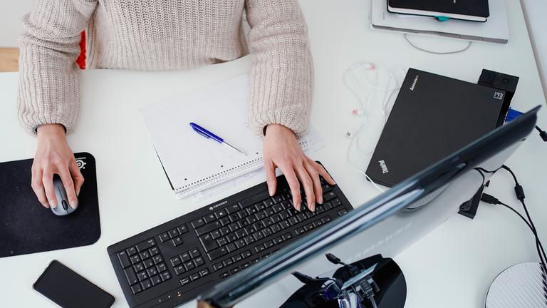 Eine Frau arbeitet an einem Stehtisch und betätigt die Maus und Tastatur eines Computers.