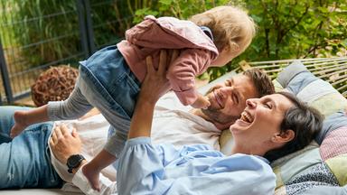 Nicolina und Martin liegen mit der einjährigen Adoptivtochter in der Hängematte.