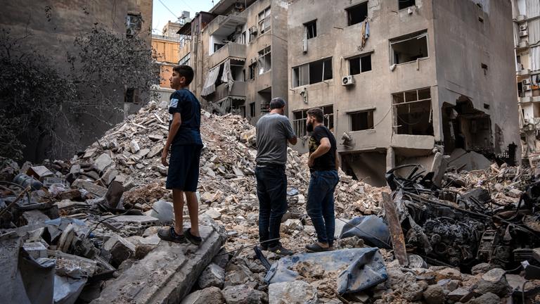 Ein Junge und zwei Männer stehen auf den Trümmern eines Gebäudes, das durch israelischen Beschuss eingestürzt ist.