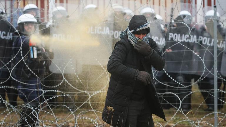 Eine Frau verfängt sich im Stacheldraht und wird von der Grenzpolizei mit Pfefferspray am Weiterkommen gehindert.