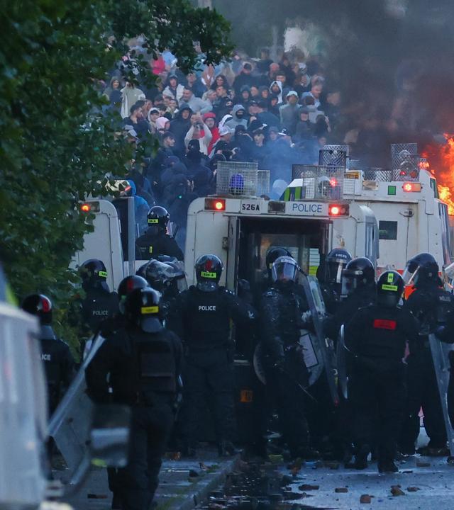 10.06.2026, Großbritannien, Belfast: Die Polizei versucht, Demonstranten in der Nähe von Newtownabbey nach einem Messerangriff am Montagabend zu räumen.