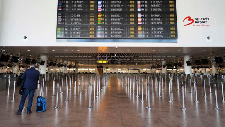 A man stands with luggage in front of a departure board full of cancellations, during a general strike, at Brussels International Airport in Zaventem