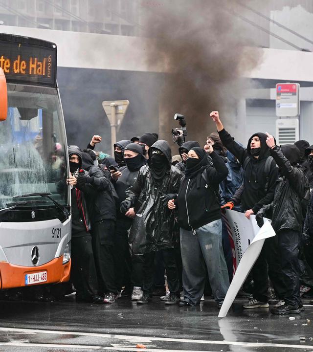 Demonstranten suchen am 9. Oktober 2026 während einer von Gewerkschaften organisierten Demonstration gegen die Haushaltsmaßnahmen der Bundesregierung in der Nähe des Bahnhofs Brüssel-Süd Schutz hinter einem Bus.