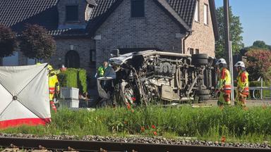 Der verunfallte Bus an einem Bahnübergang, auf dem Foto sind zwei Feuerwehrleute zu sehen, links ist ein Sichtschutzzelt. 