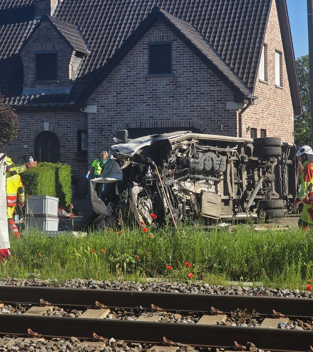 Der verunfallte Bus an einem Bahnübergang, auf dem Foto sind zwei Feuerwehrleute zu sehen, links ist ein Sichtschutzzelt. 