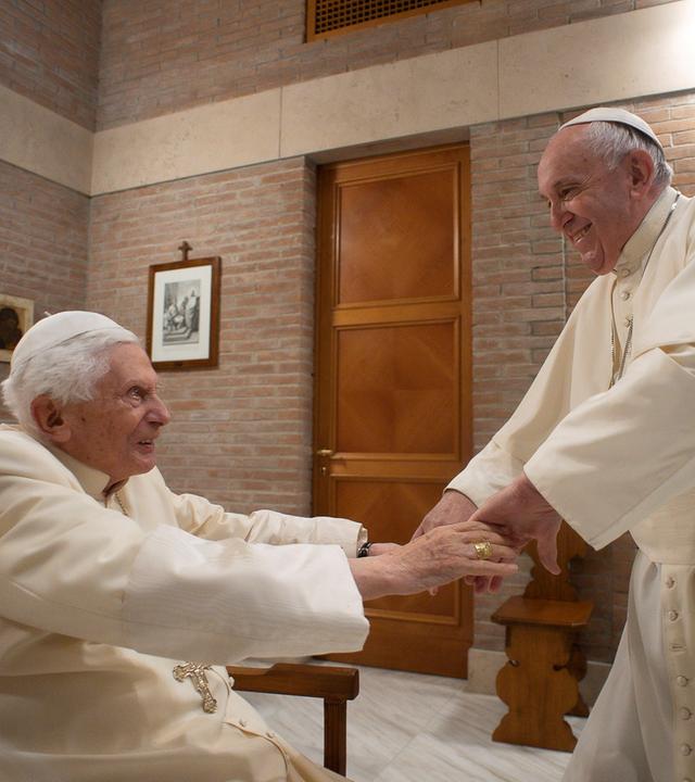 Papst Benedikt XVI. und Papst Franziskus reichen sich die Hände im Vatikan.