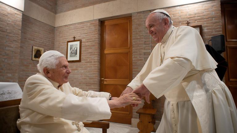 Papst Benedikt XVI. und Papst Franziskus reichen sich die Hände im Vatikan.
