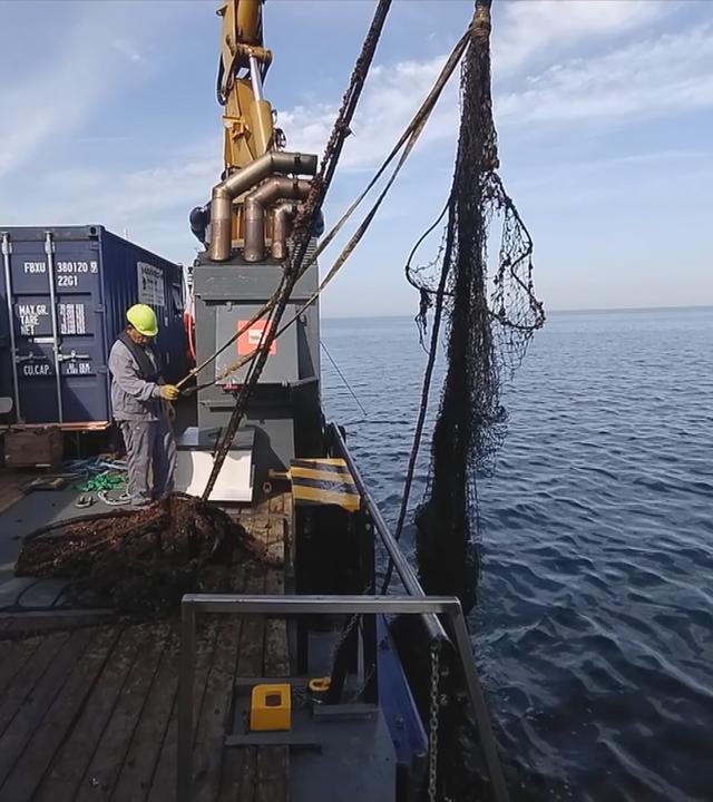 Auf dem Bild sieht man die Bergung eines Geisternetzes aus dem Wasser.