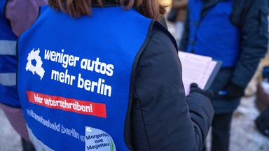 Der Rücken einer Person, die ein blaues Leibchen mit der Aufschrift "weniger autos - mehr berlin - hier unterschreiben!" trägt.